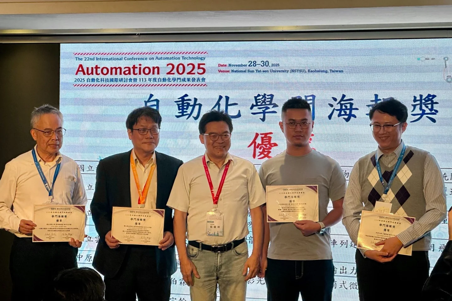 五位得獎人手持獎狀，站在 Automation 2025 學門海報獎的投影幕前。