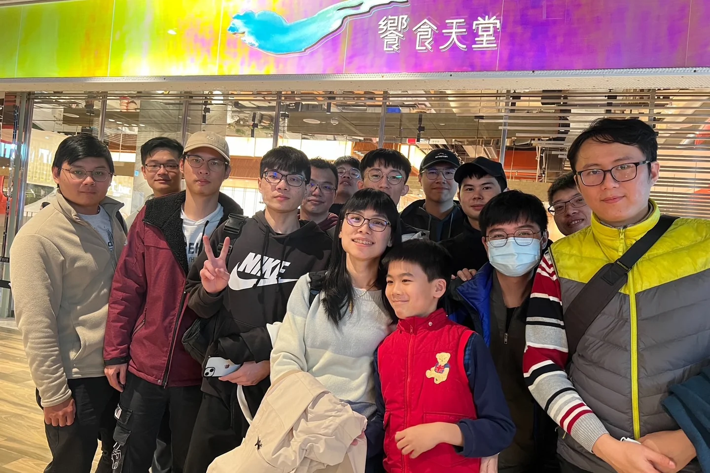 餐廳入口前合影，十餘位成員站成兩排，前排中間有一位孩童。