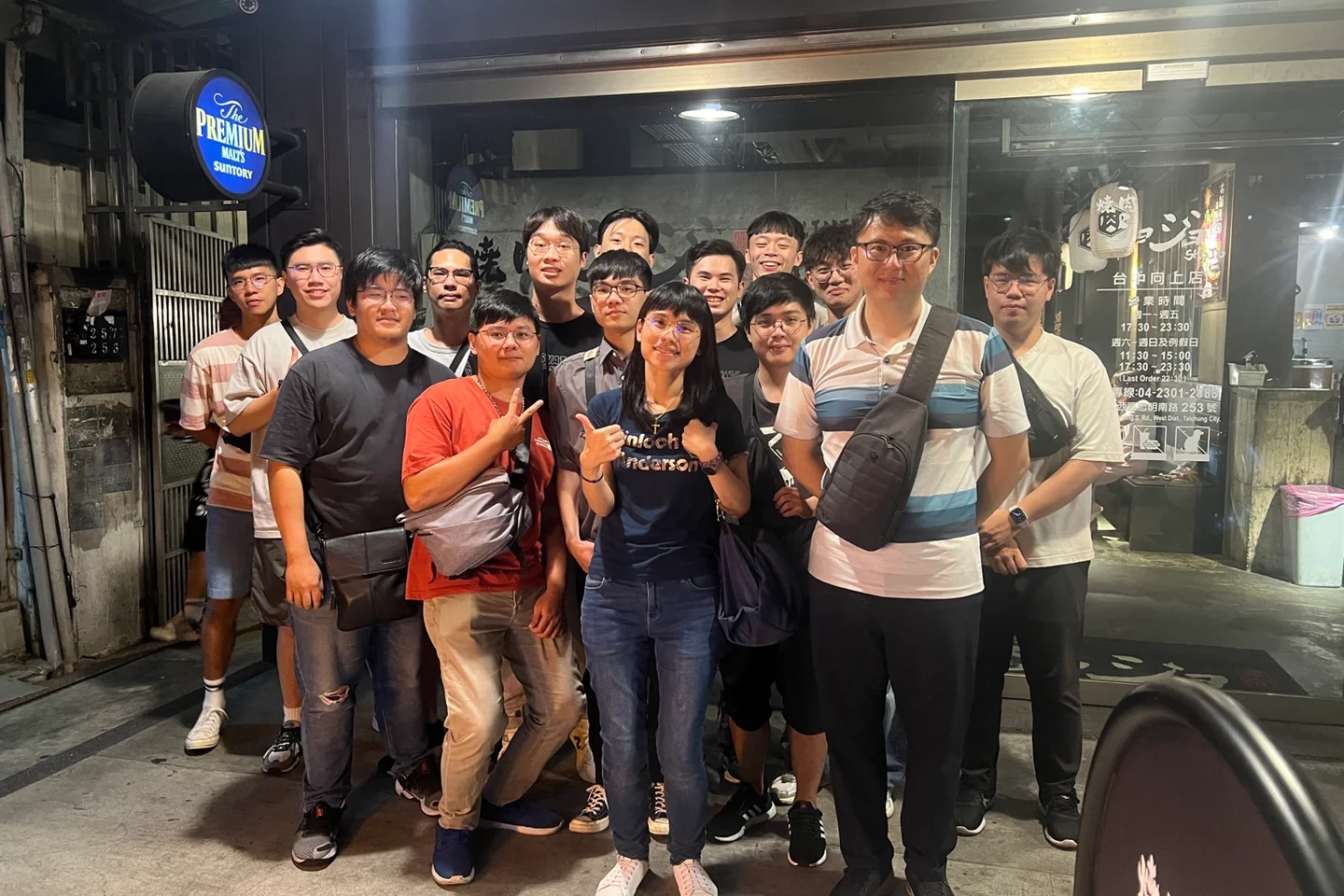 夜間店門口合影，十餘位成員分前後兩排站立，招牌與燈籠亮著。