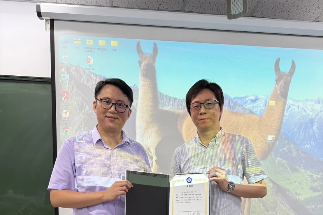教室講台前兩人共同持攤開的感謝狀合影，背後是投影幕與黑板。